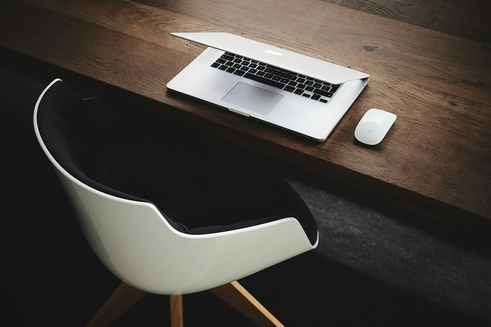 Ordinateur portable et souris posés sur un bureau en bois, chaise design blanche