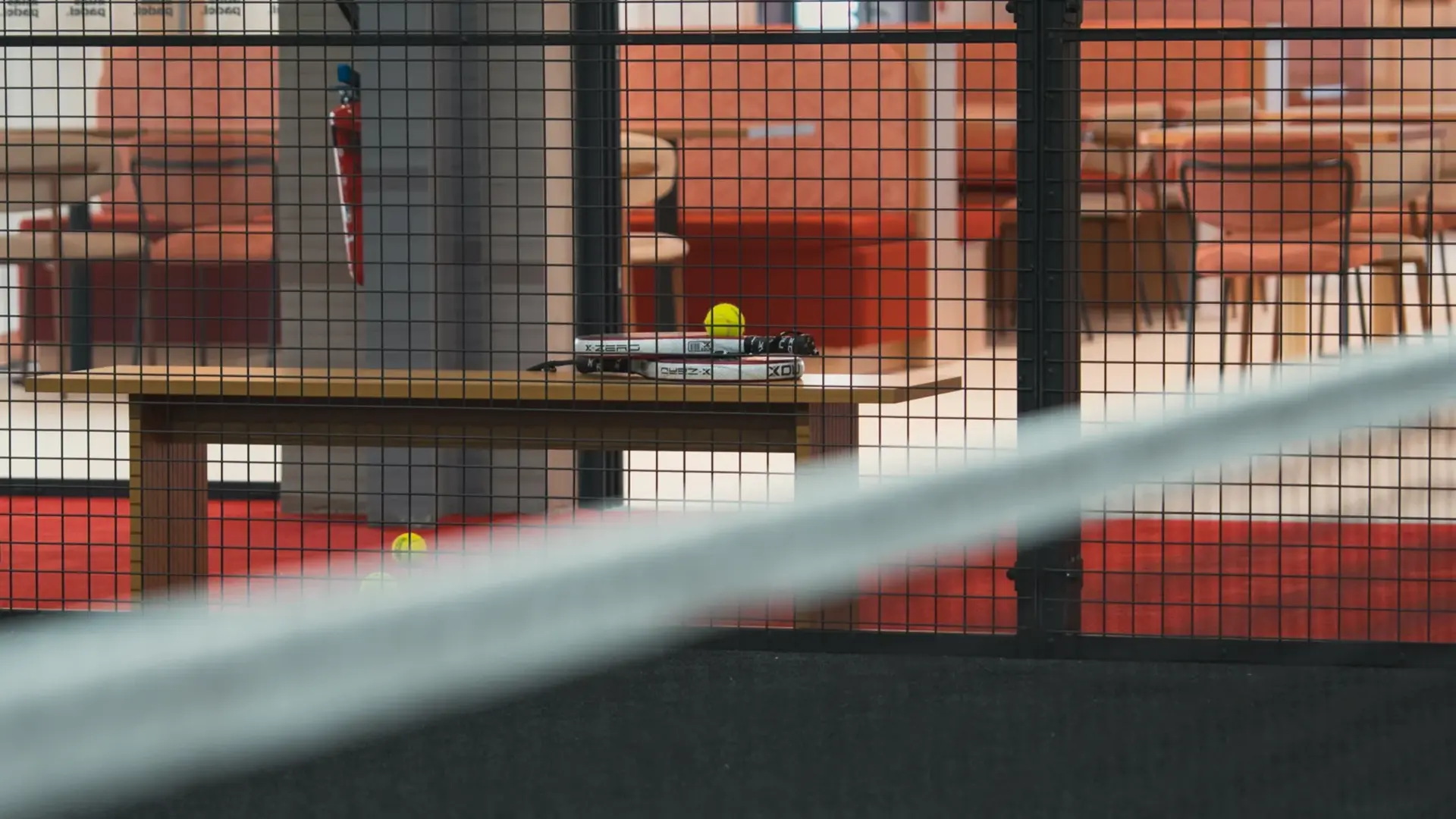 Raquettes et balles de padel derrière la grille d'un terrain, réalisation Atlas Padel